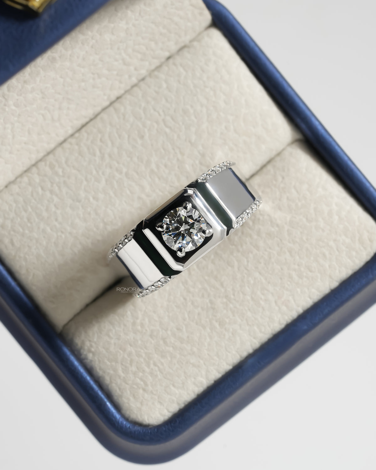 Men's round lab grown diamond ring in white gold resting in a navy and cream ring box, top view