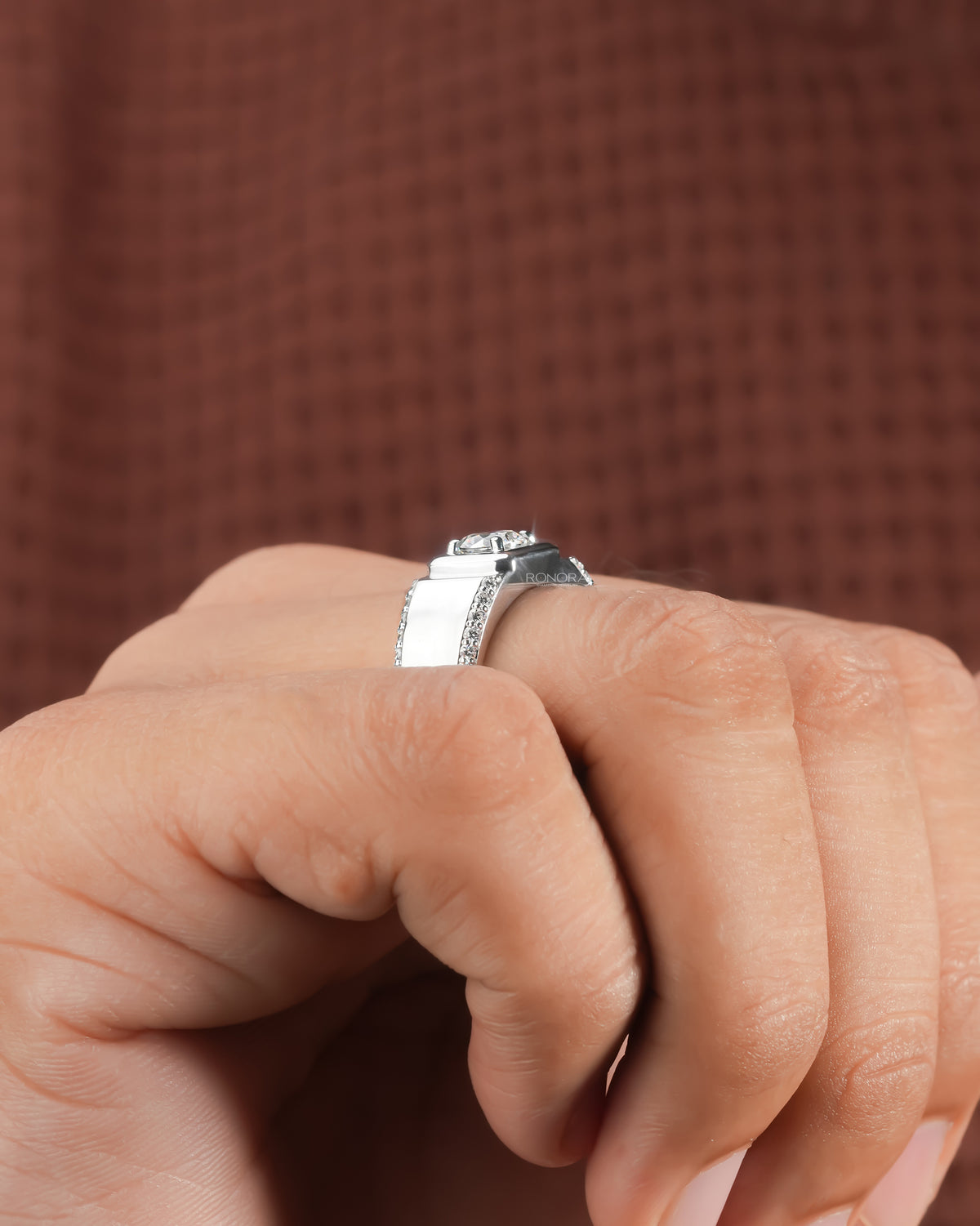 Side view of a men's round lab grown diamond ring in white gold worn on a hand against a brown backdrop