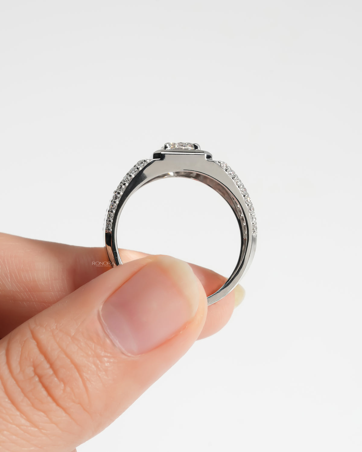 Side view of a men's round lab grown diamond ring in white gold with a wide pave band, held between fingers