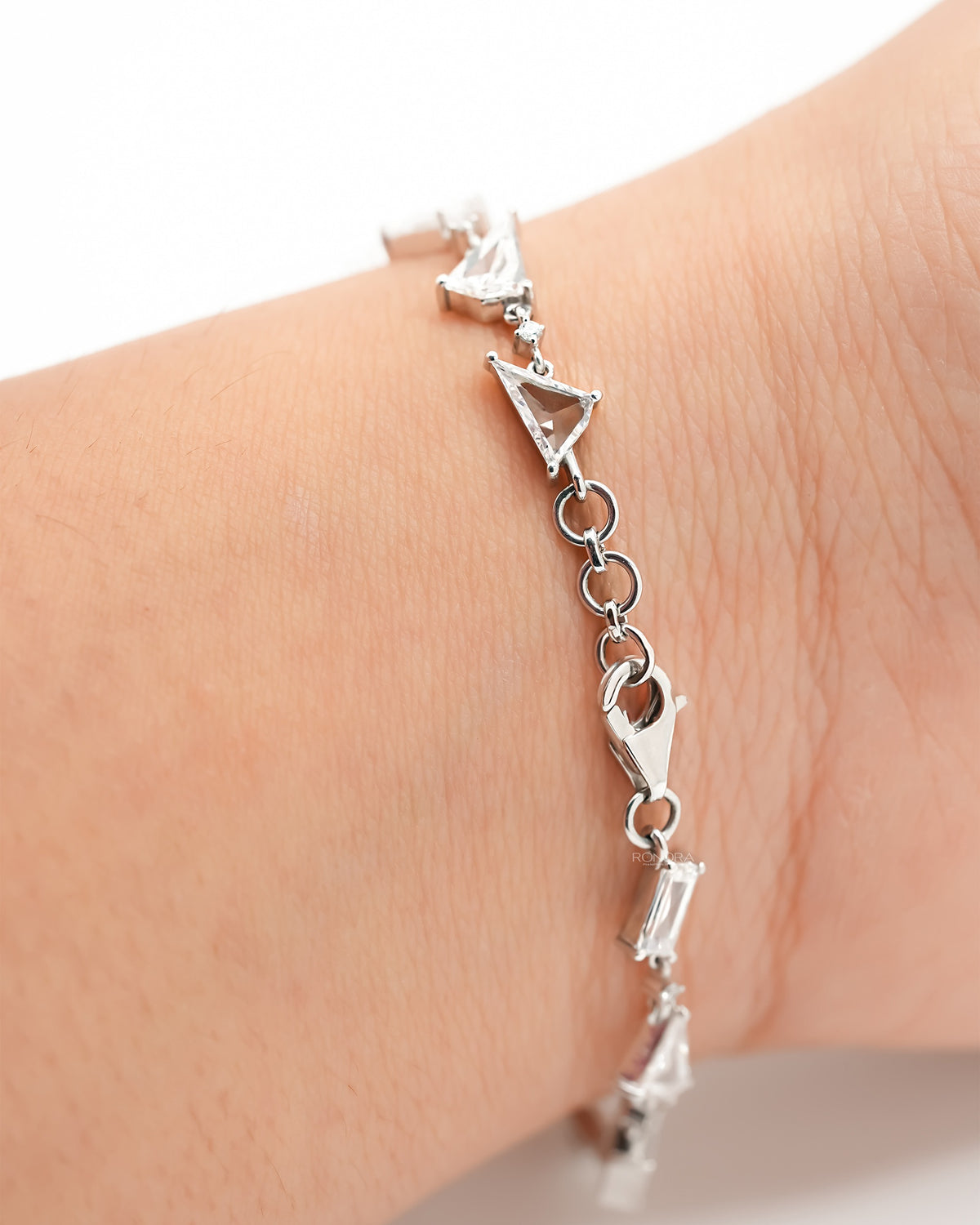Multi shape lab grown diamond bracelet in white gold on a wrist, showing triangle and baguette stones and the clasp