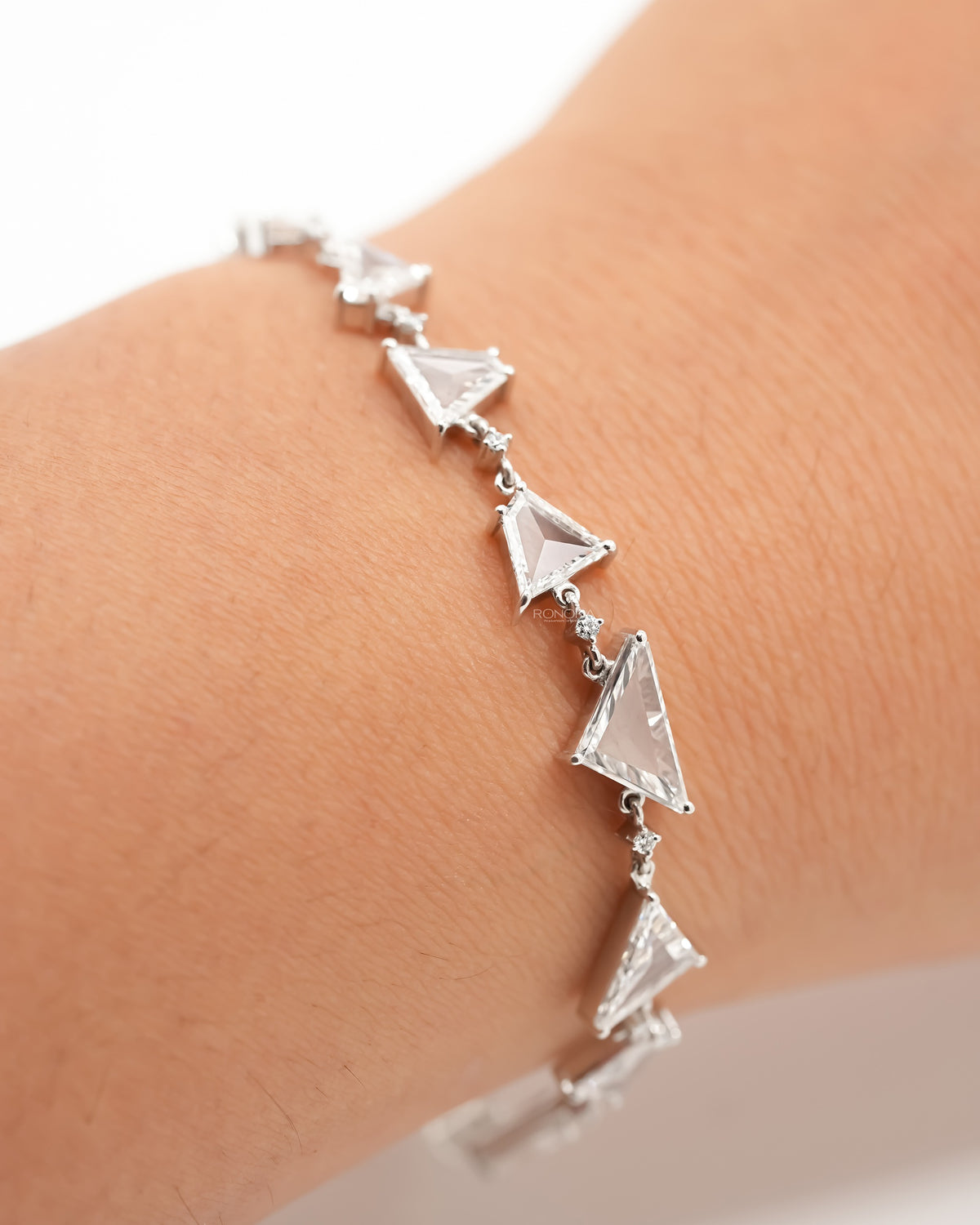 Wrist wearing a multi shape lab grown diamond bracelet in white gold with triangle stones and small round accents