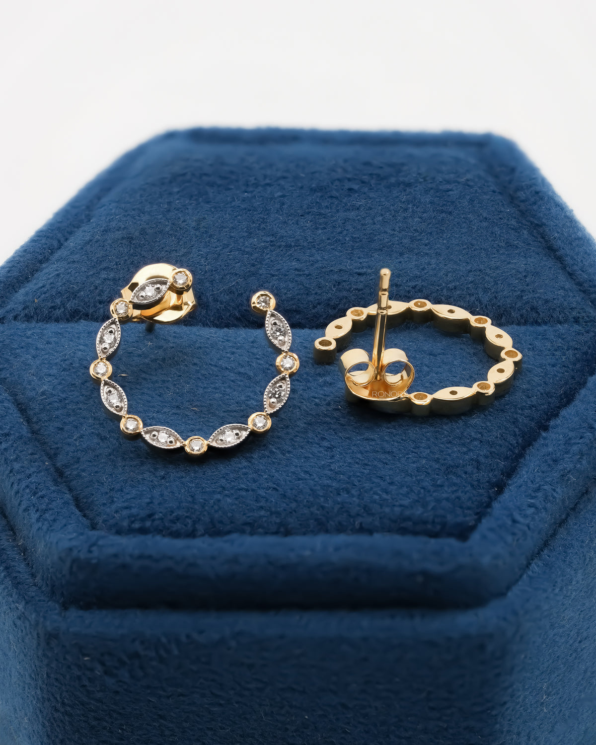 Open circle lab grown diamond earrings in a blue velvet hex box held in a hand against a bright background