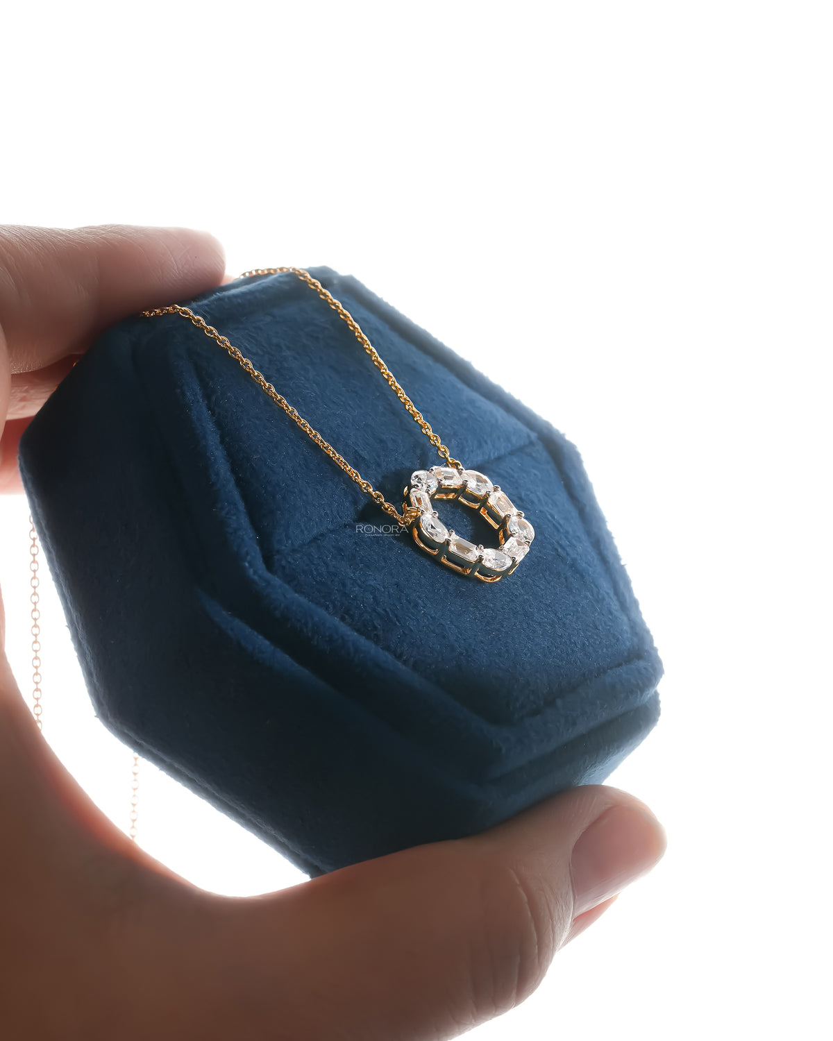 Angled view of an open circle lab grown diamond pendant necklace resting in a blue velvet jewelry box