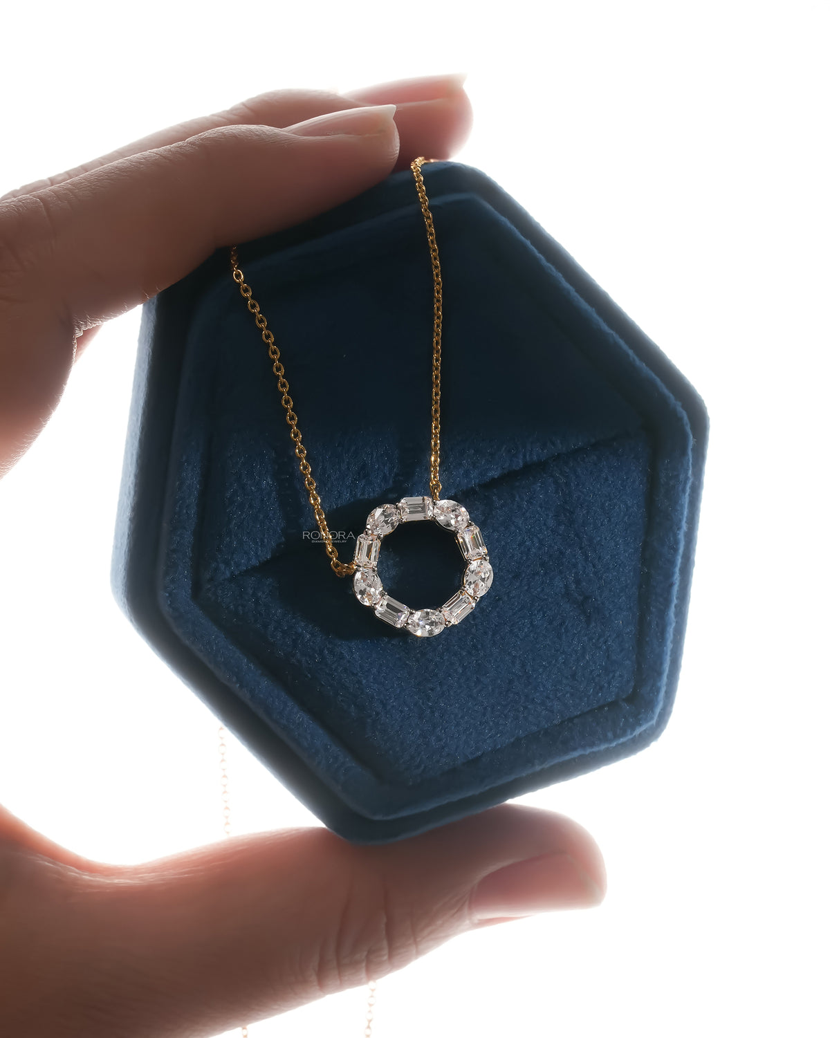 Open circle lab grown diamond pendant with oval and emerald cut stones in a backlit hexagonal jewelry box