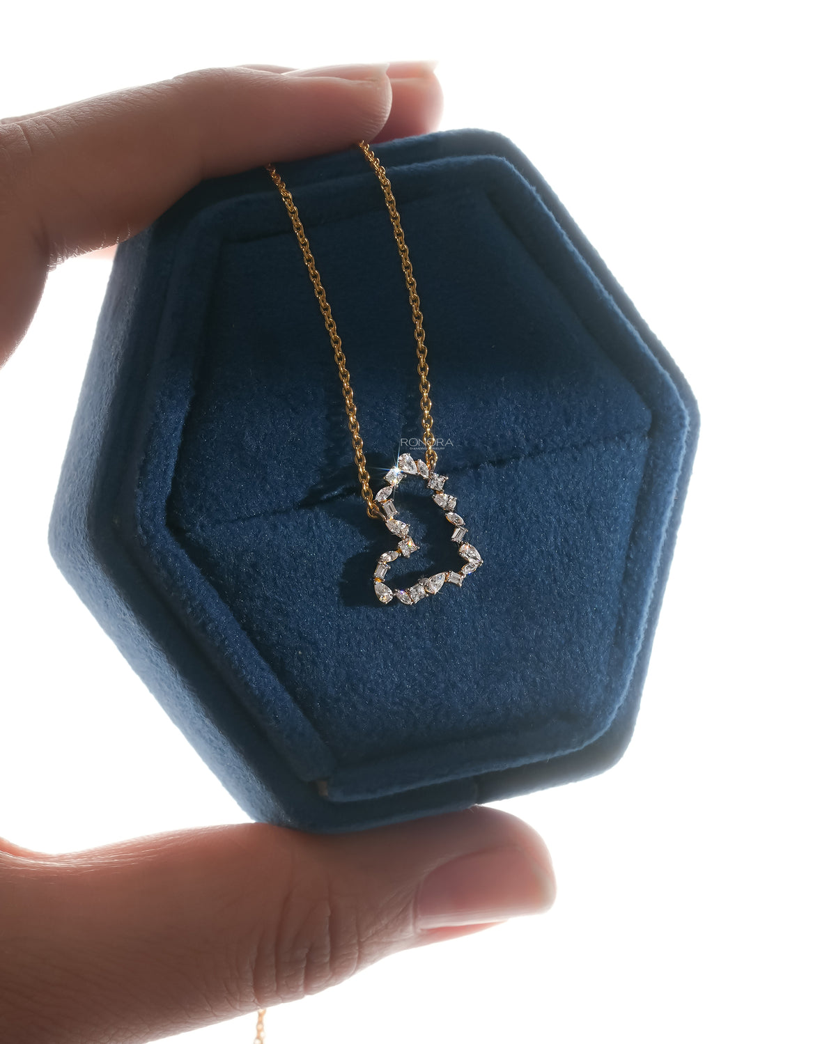 Open heart lab grown diamond pendant with pear and emerald cut stones in a backlit hexagonal jewelry box