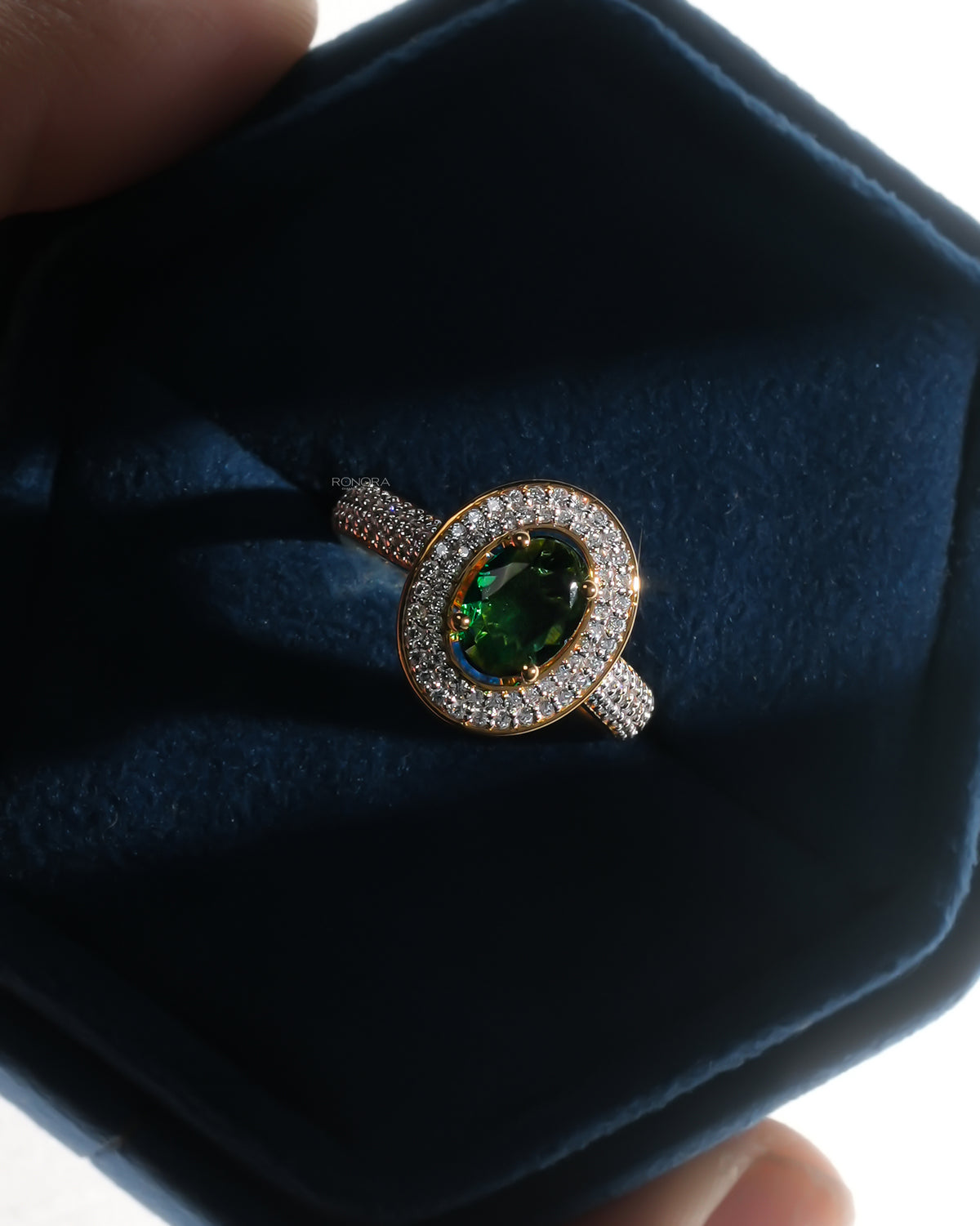 Oval green stone double halo ring with a pave band in a dark blue velvet ring box, front view with soft glow