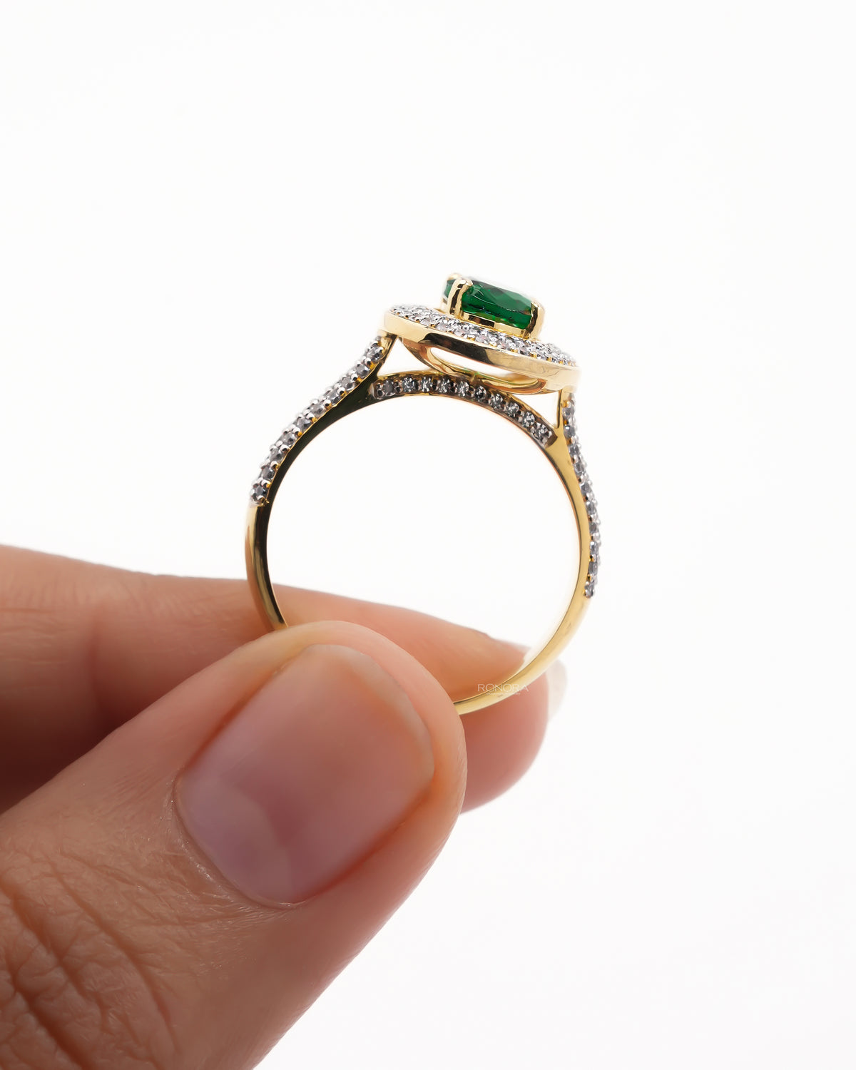Yellow gold oval green double halo ring held upright between fingers, showing the pave shank and under gallery