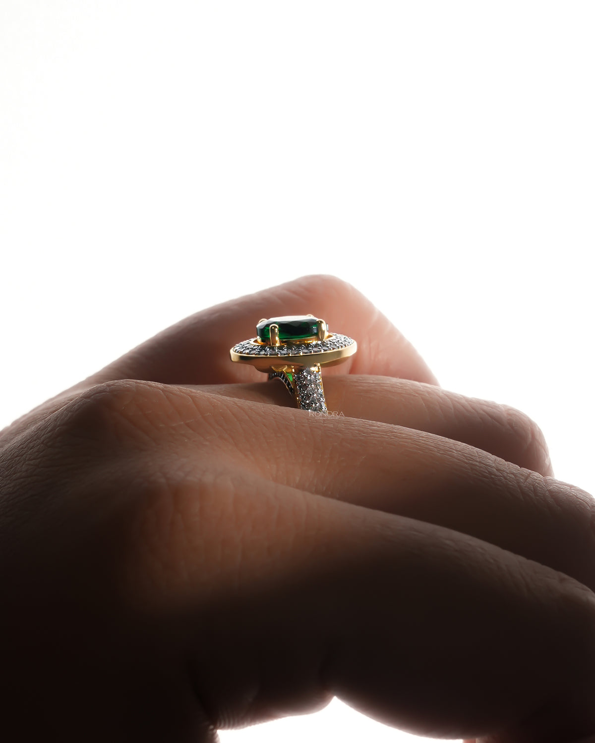Side view of an oval green double halo ring in yellow gold worn on a hand, pave band visible