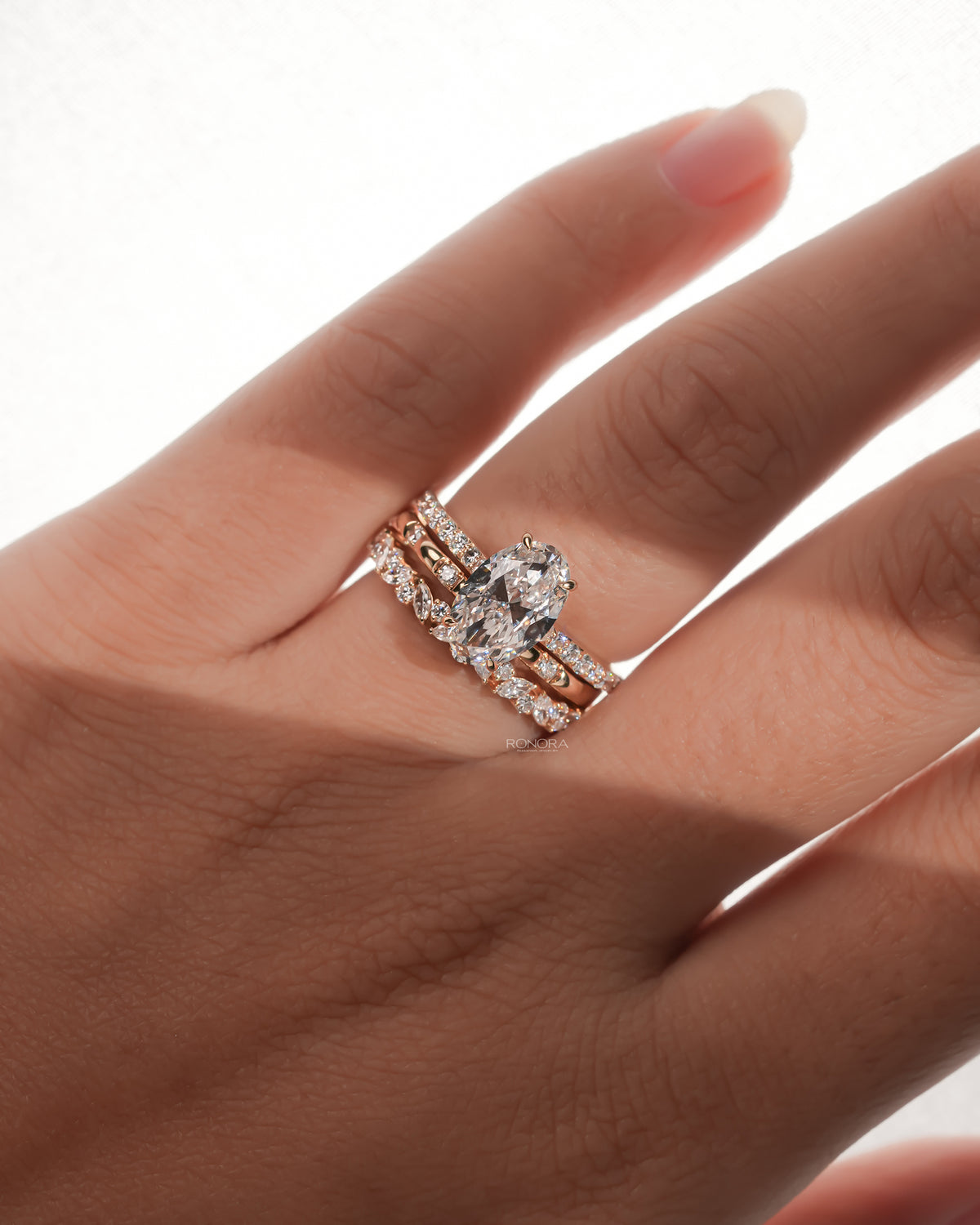 Hand wearing an oval lab grown diamond bridal set, oval solitaire stacked with two diamond bands