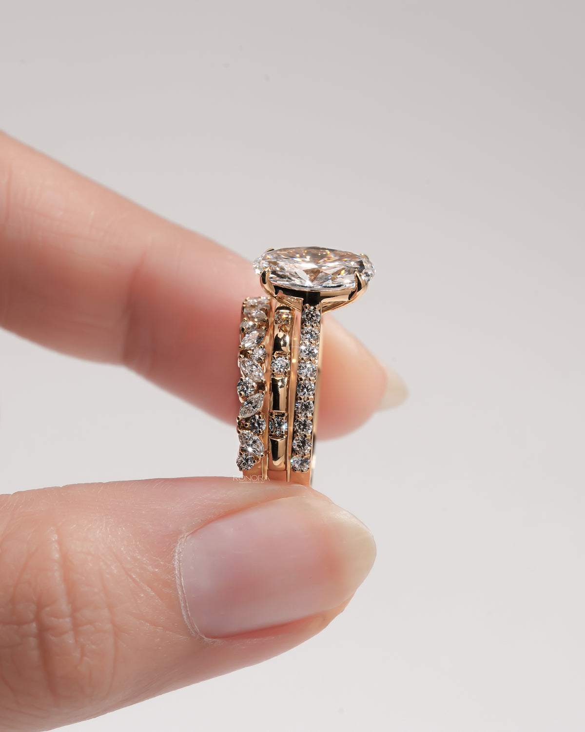 Side view of an oval lab grown diamond bridal set held between two fingers, showing the three stacked rings