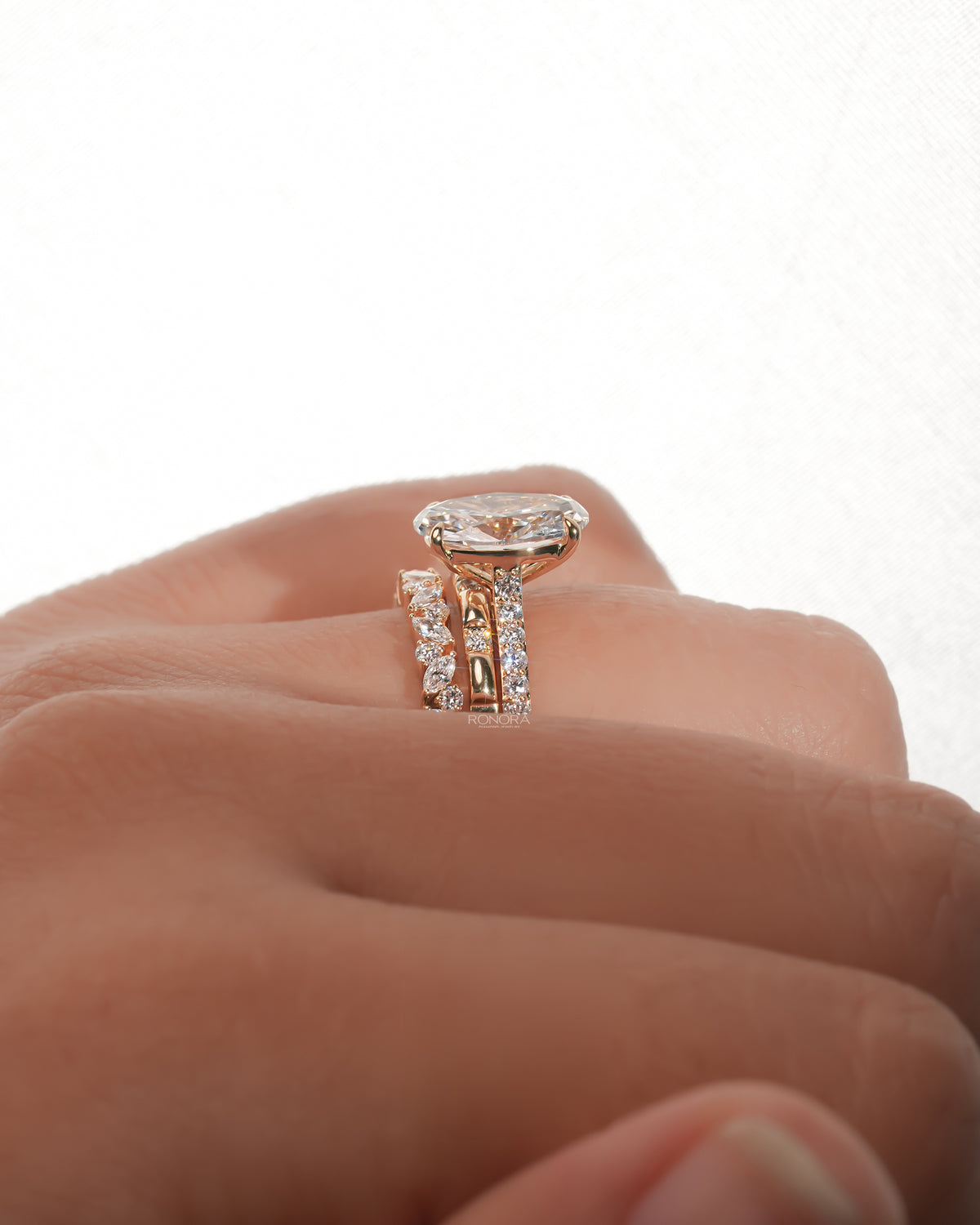 Side view of an oval lab grown diamond bridal set worn on a finger, solitaire ring stacked with two diamond bands