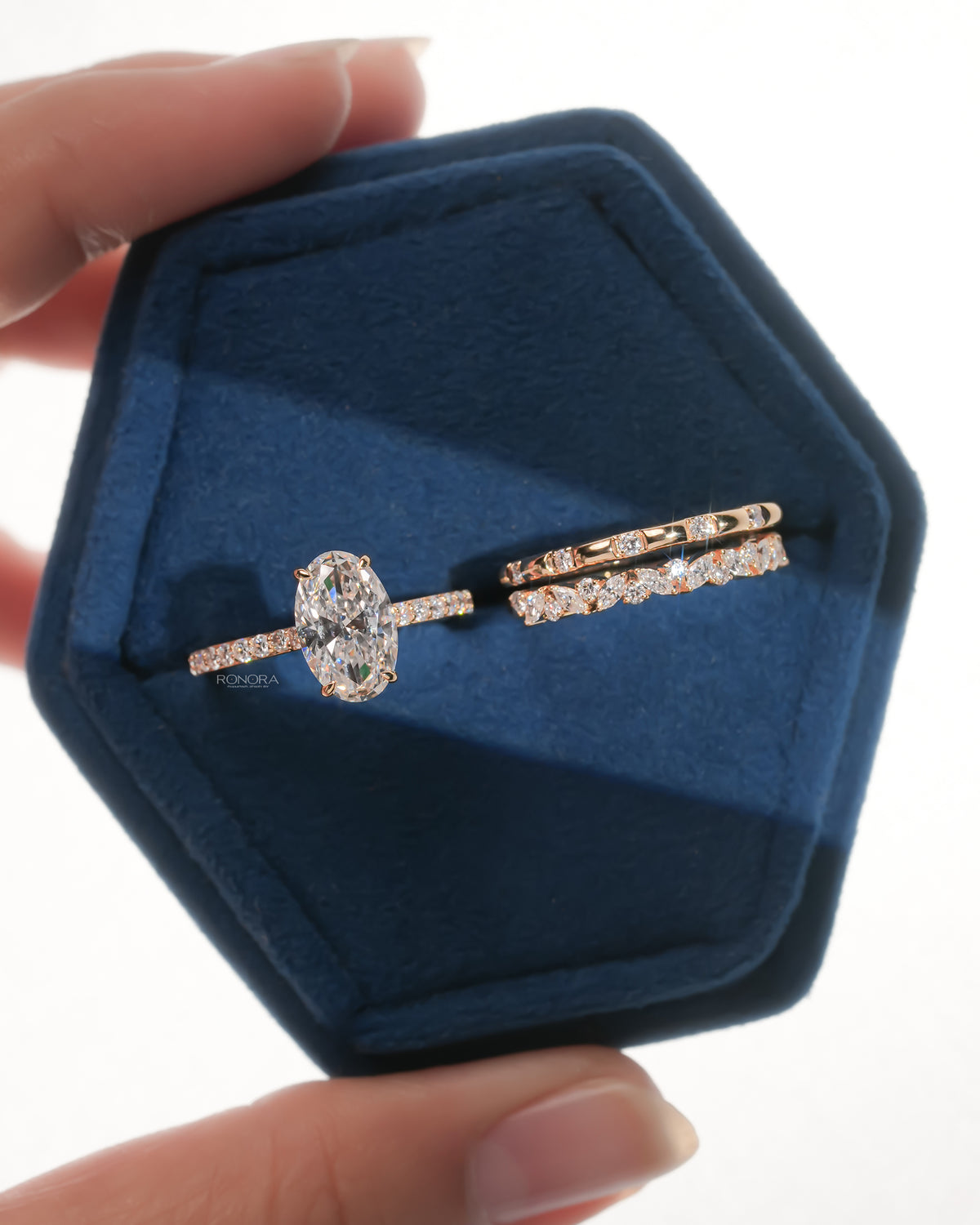 Rose gold bridal set: an oval lab grown diamond solitaire with a pave band beside two matching stacking bands, in a navy velvet box