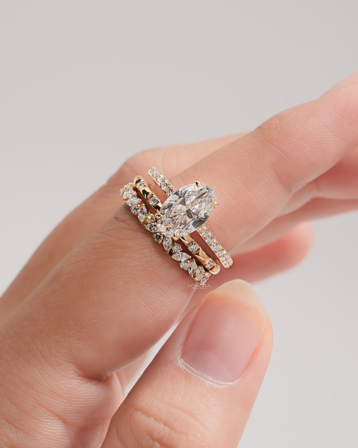 Close-up of an oval lab grown diamond bridal set in yellow gold on a fingertip, solitaire with two diamond bands