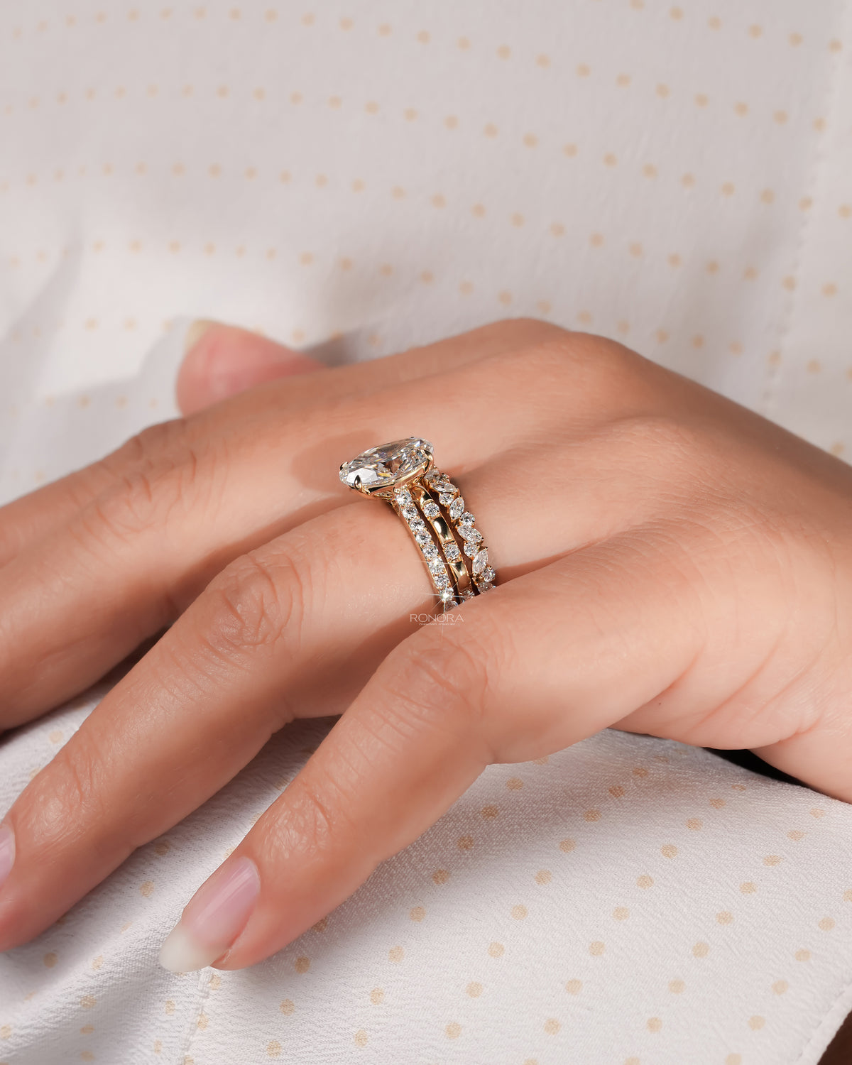 Oval lab grown diamond bridal set in yellow gold on a hand resting on cream dotted fabric, side view