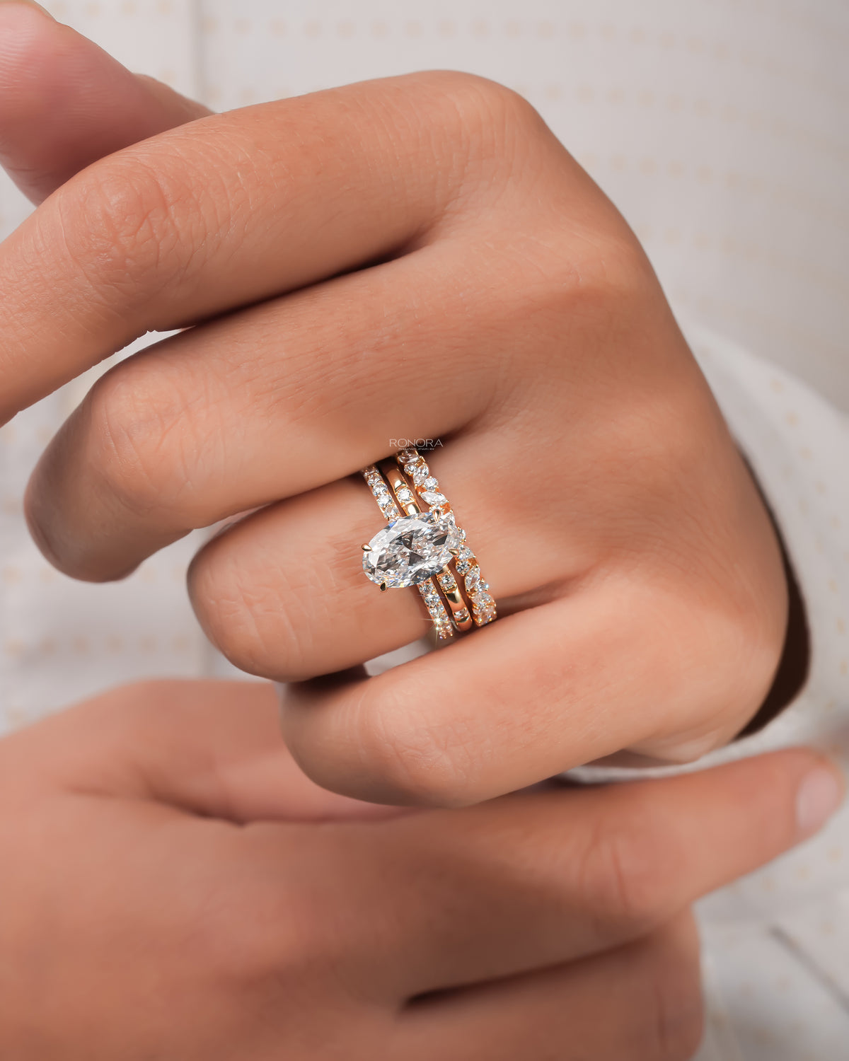 Hand wearing an oval lab grown diamond bridal set in yellow gold, solitaire ring with two matching stacked bands