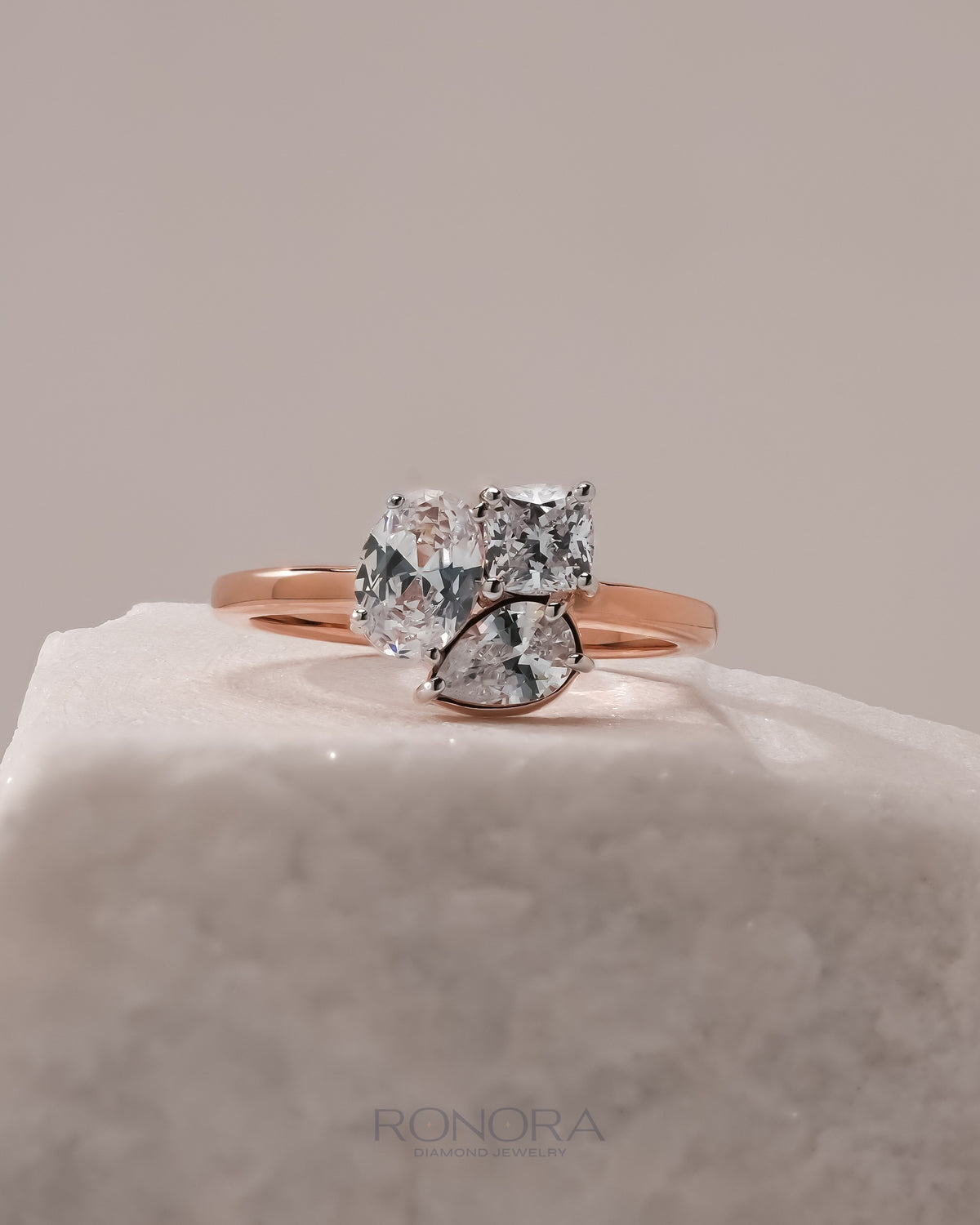 Oval lab grown diamond cluster ring in rose gold with oval, cushion and pear stones grouped together on white stone