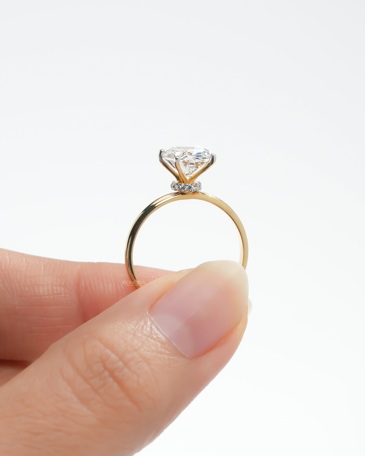 Close-up of an oval lab grown diamond hidden halo ring held between fingers, showing the halo and slim yellow gold band