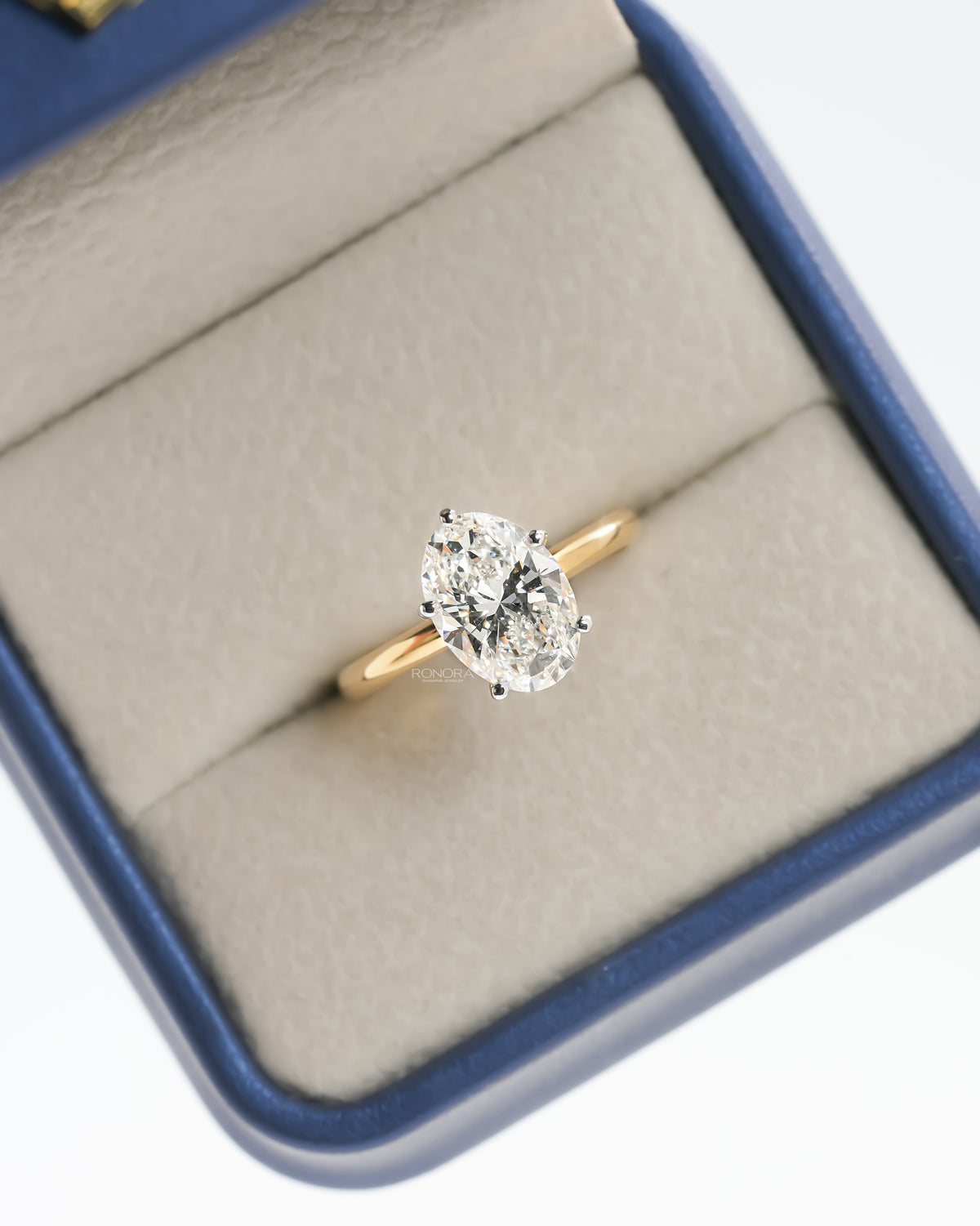 Oval lab grown diamond hidden halo ring with a yellow gold band in a blue ring box, top view