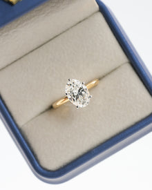 Oval lab grown diamond hidden halo ring with a yellow gold band in a blue ring box, top view