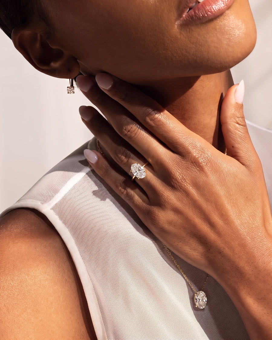 Model's hand at her neck wearing an oval lab grown diamond hidden halo ring in yellow gold with an oval pendant