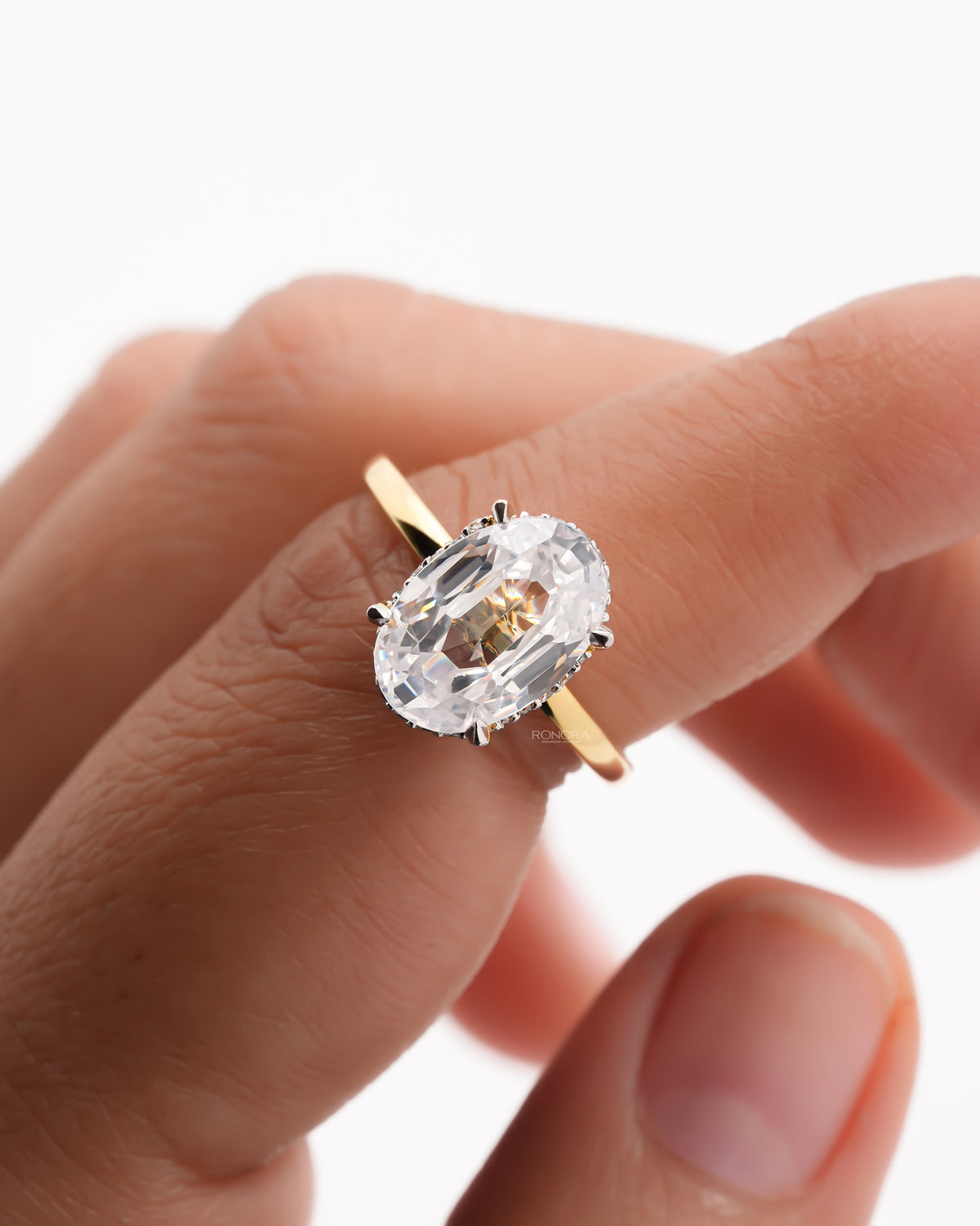 Close-up of a 2 carat oval moissanite hidden halo ring on a finger with a yellow gold band and claw prongs