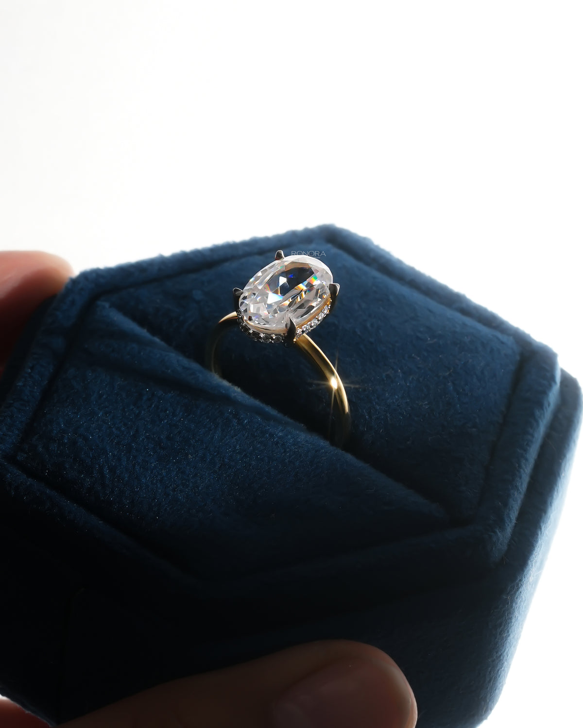 Angled view of an oval moissanite hidden halo ring in a navy velvet ring box, showing the halo under the stone
