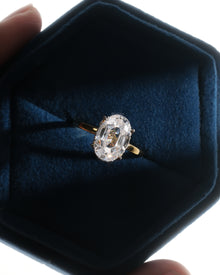 Oval moissanite hidden halo ring with a yellow gold band resting in a navy velvet ring box held in hand