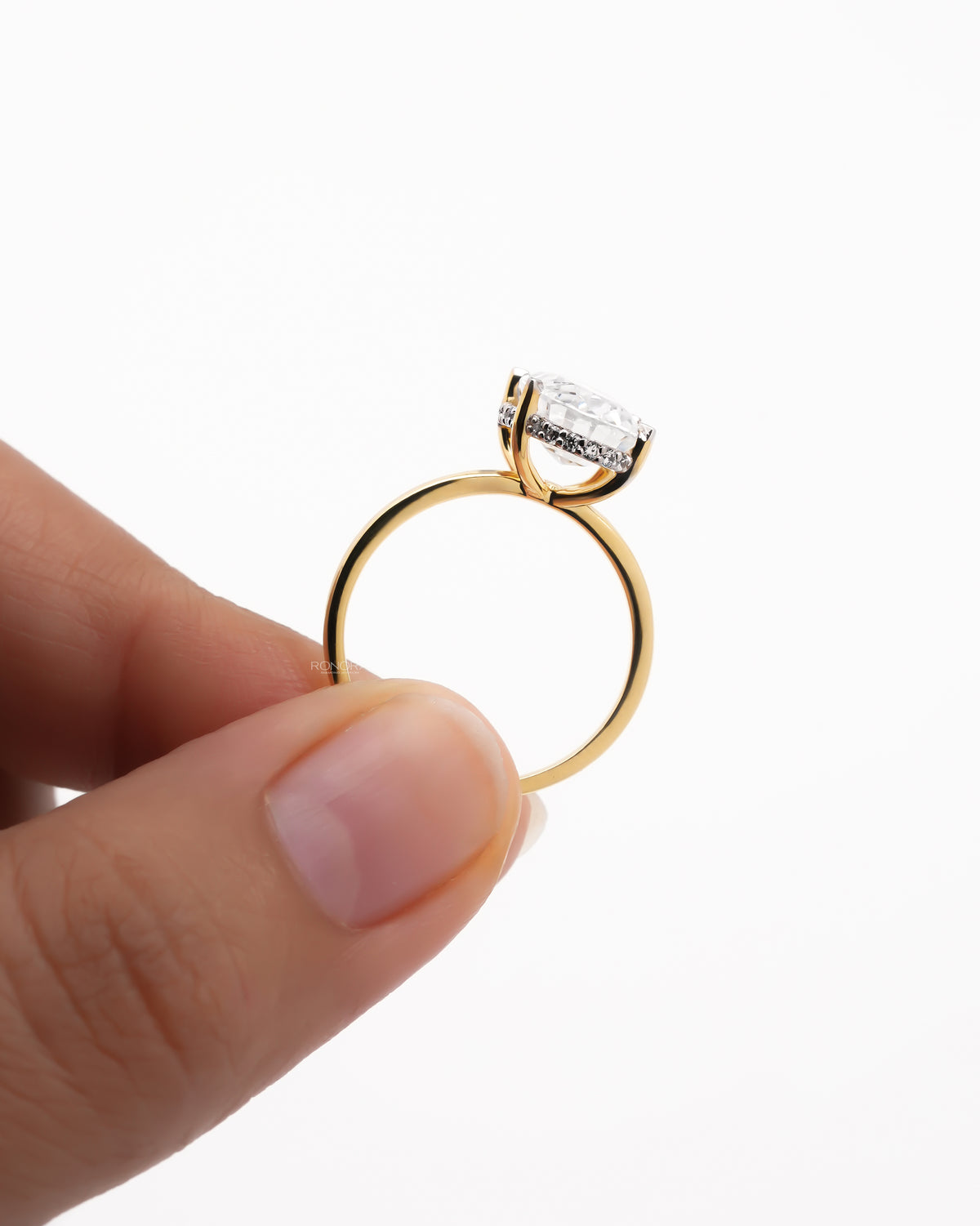 Yellow gold oval moissanite hidden halo ring held upright between fingers, showing the hidden halo and thin band