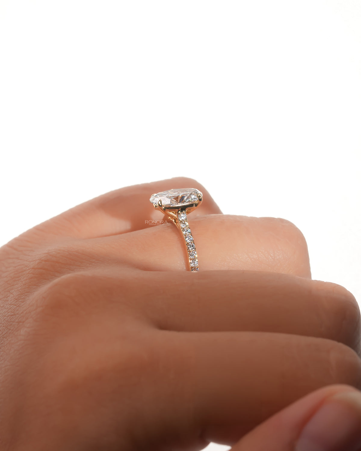 Side view of an oval pave lab grown diamond engagement ring on a finger, showing the prongs and pave band
