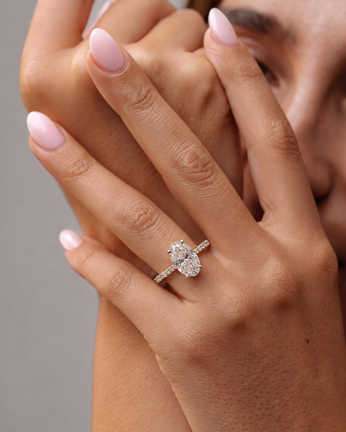 Model wearing an oval pave lab grown diamond engagement ring with a slim pave band, hands raised to her face
