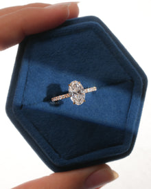Top view of an oval pave lab grown diamond engagement ring in a blue velvet hexagon ring box held in hand