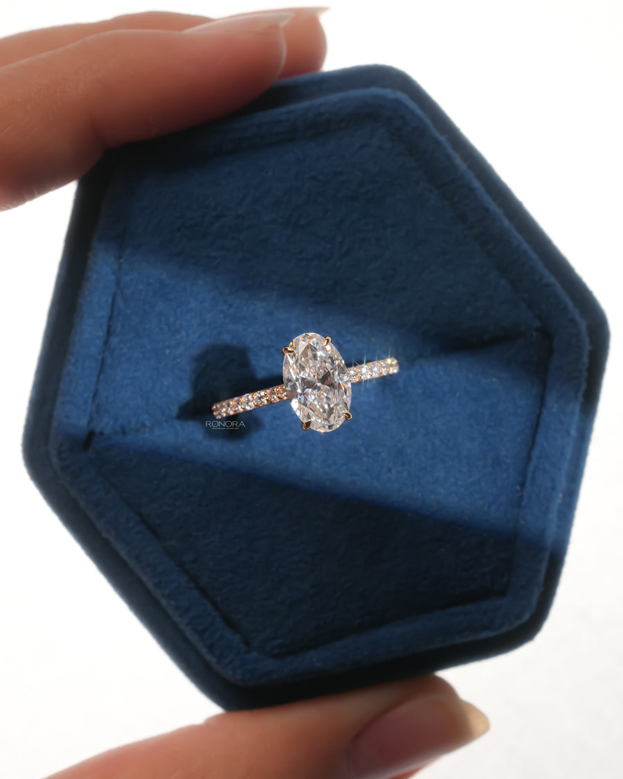 Top view of an oval pave lab grown diamond engagement ring in a blue velvet hexagon ring box held in hand
