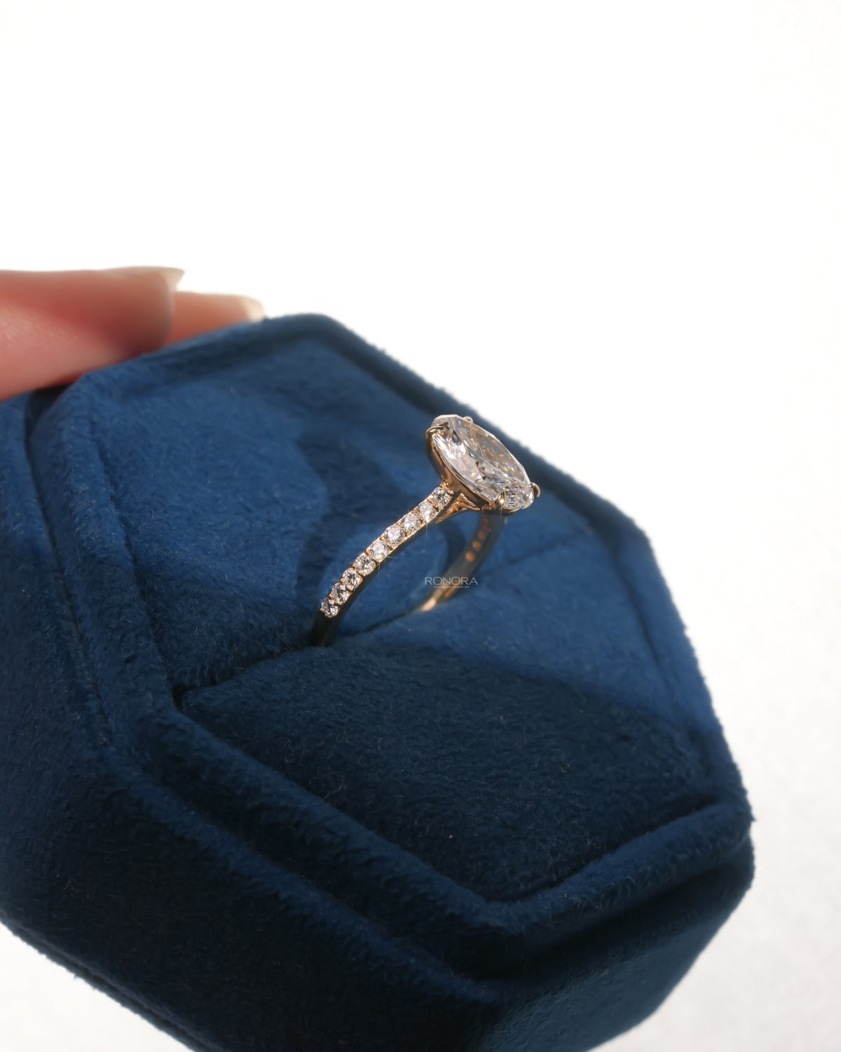 Oval pave lab grown diamond engagement ring resting in a blue velvet ring box, angled view of the pave band