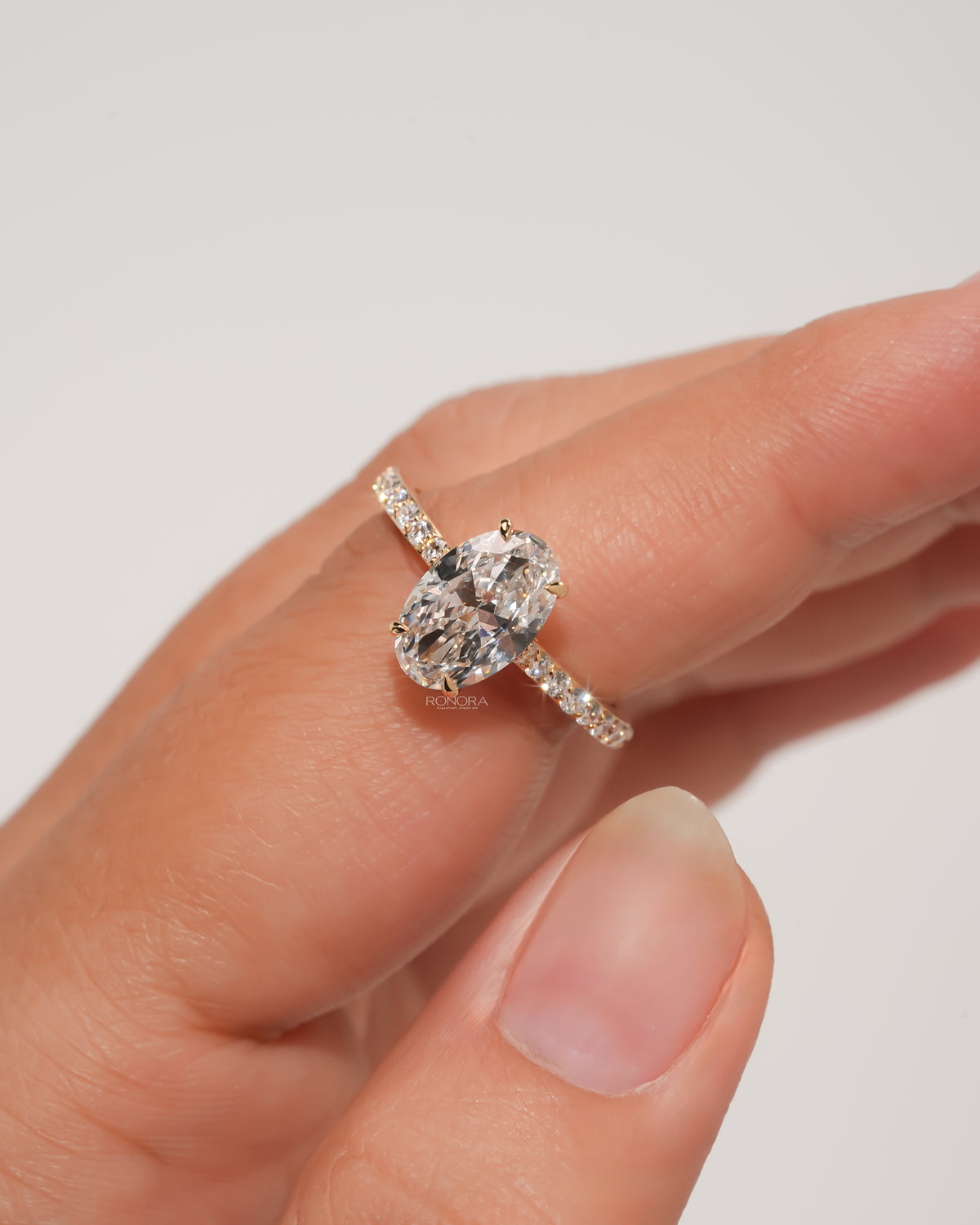 Close-up of an oval pave lab grown diamond engagement ring in yellow gold worn on a finger held out by hand