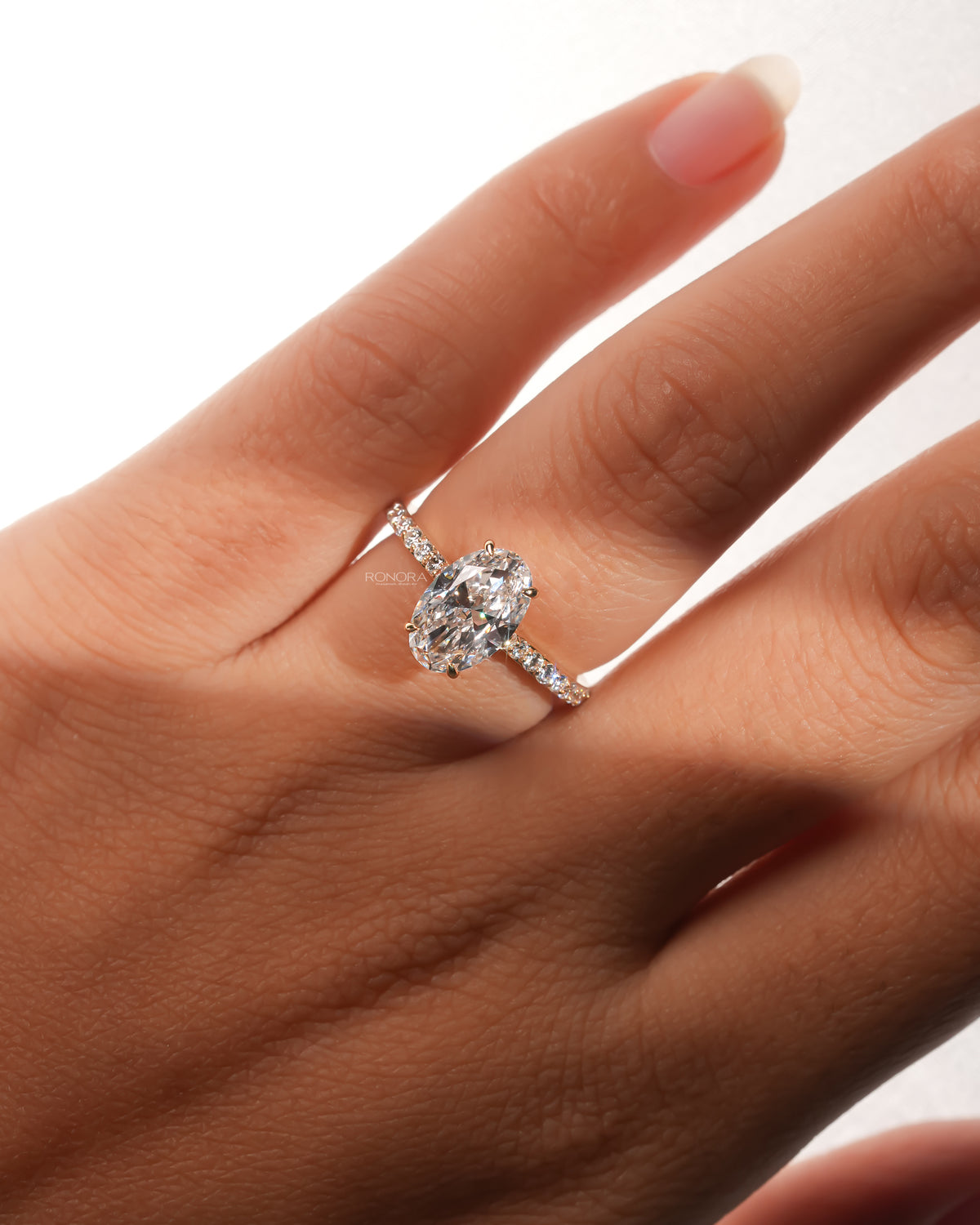 Hand wearing an oval pave lab grown diamond engagement ring in yellow gold with a diamond-set pave band