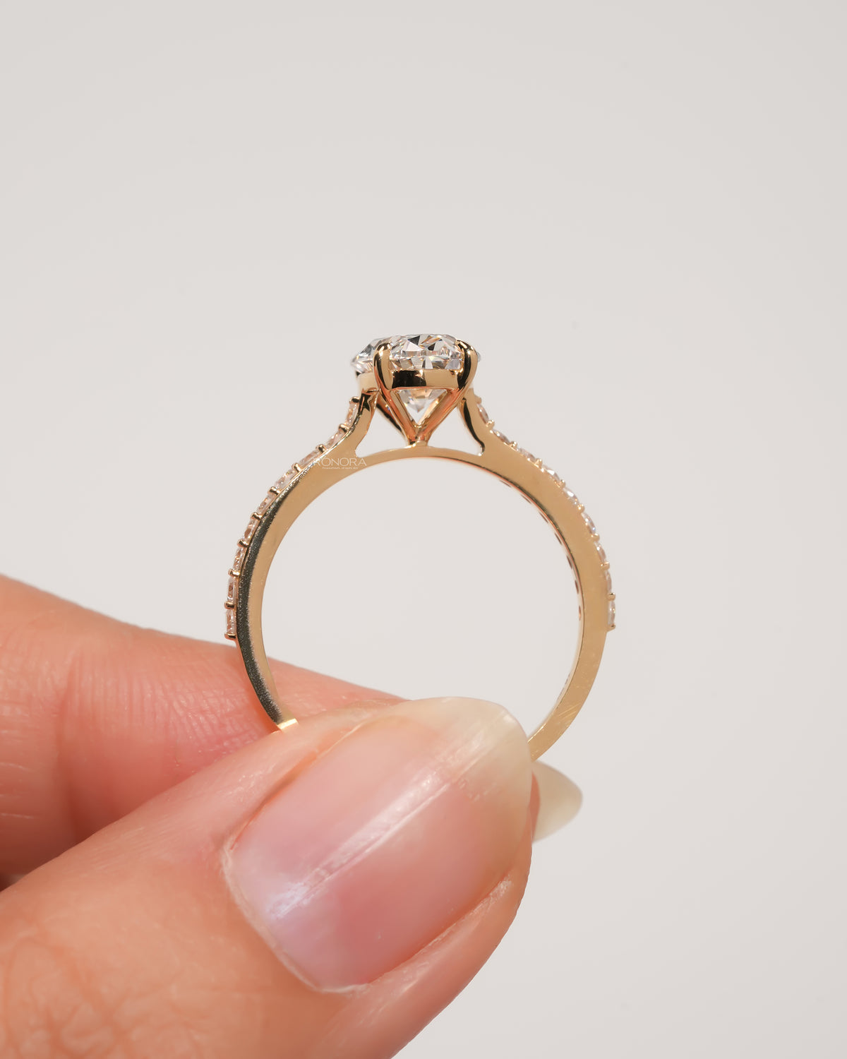 Oval pave lab grown diamond engagement ring in yellow gold held between two fingers, side profile of the pave band