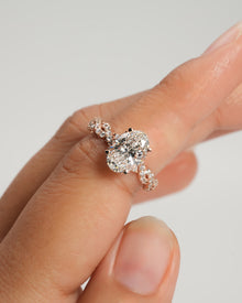 Oval lab grown diamond ring in rose gold with twisted pave band, held between fingertips against a plain grey backdrop