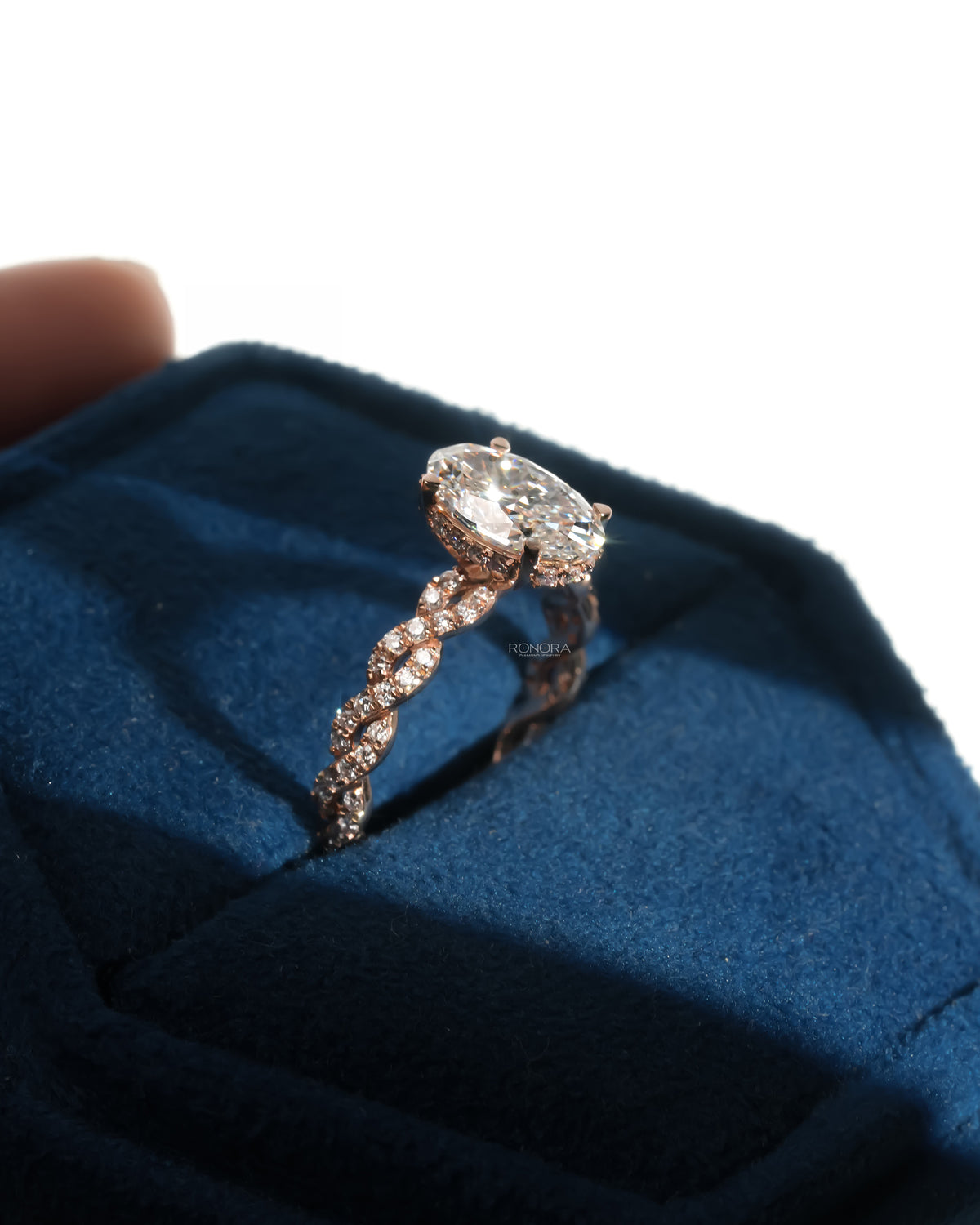 Oval lab grown diamond ring in rose gold with a twisted pave band, resting in a deep blue velvet ring box in sunlight
