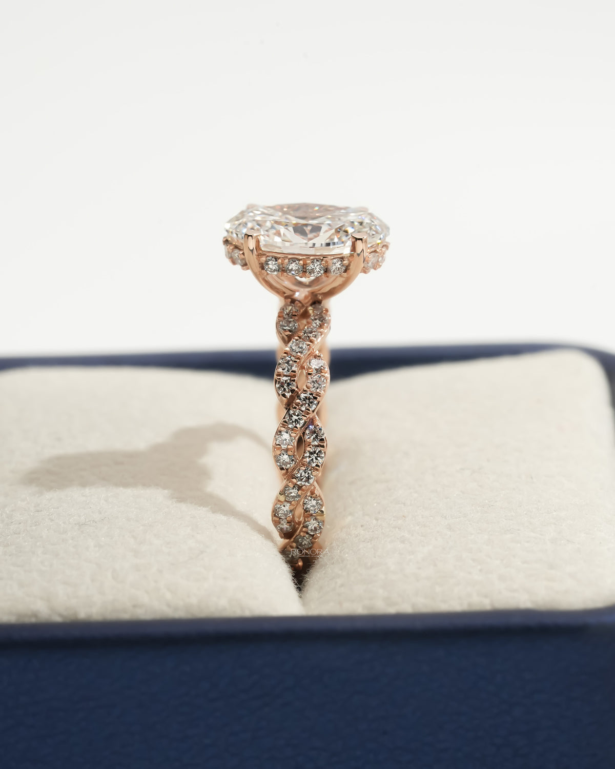 Side profile of an oval lab grown diamond ring in a jewelry box, showing the rose gold twisted pave band and diamond halo