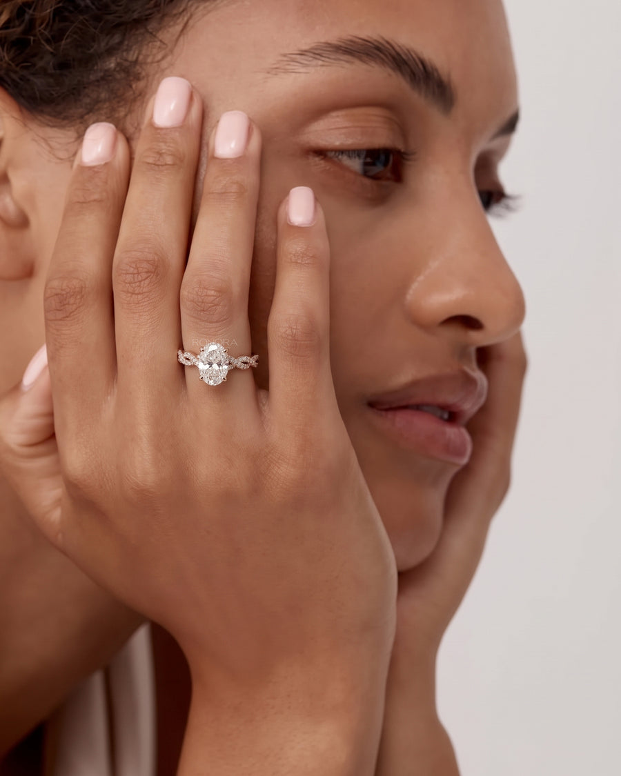 Woman with hands against her face wearing an oval lab grown diamond ring with a rose gold twisted pave band