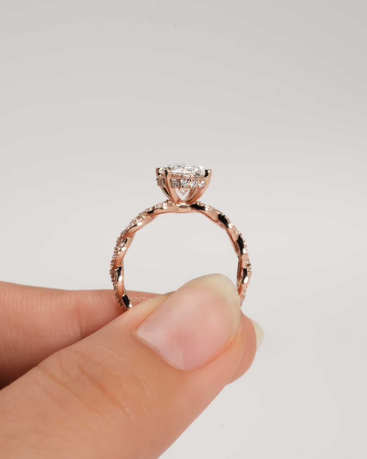 Side view of an oval lab grown diamond ring held up in fingers, rose gold twisted pave band with diamonds under the stone