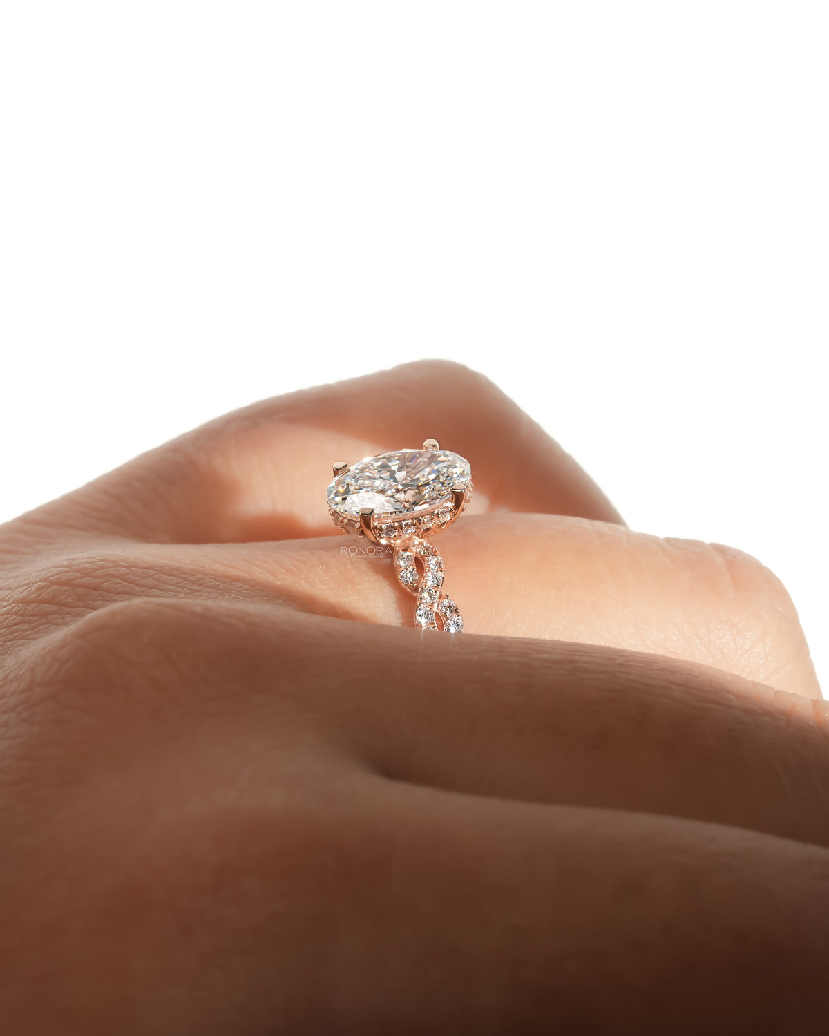 Low side angle of an oval lab grown diamond ring in rose gold with a twisted pave band, worn on a hand