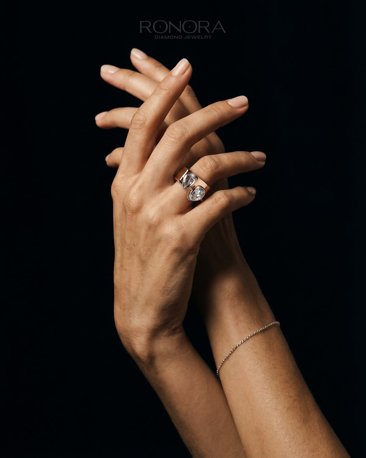 Pear lab grown diamond bypass ring with two bezel set pear stones on a wide rose gold band, worn on a hand, black backdrop