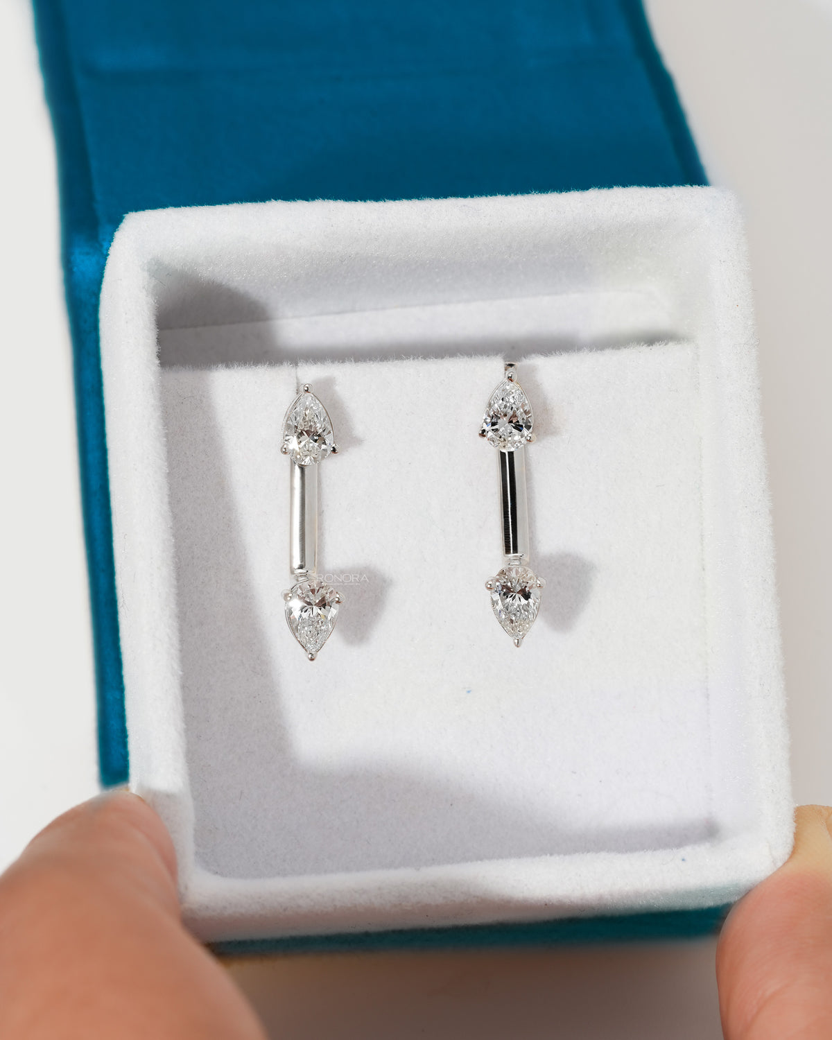 Pair of pear lab grown diamond ear jacket earrings in white gold in a white velvet box held in hand