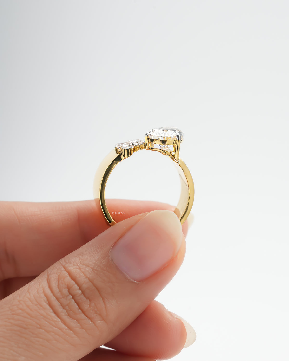 Side profile of a pear toi et moi lab grown diamond ring in yellow gold held between two fingers, open band