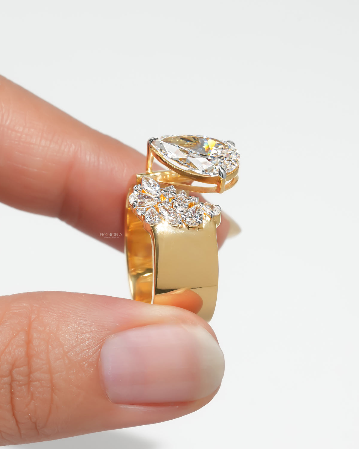 Side view of a pear toi et moi lab grown diamond ring in yellow gold with open band and cluster, held between fingers