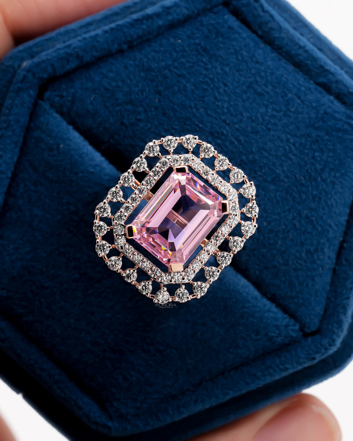 Close-up of a pink emerald cut double halo ring in rose gold in a blue velvet ring box, top view
