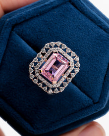 Close-up of a pink emerald cut double halo ring in rose gold in a blue velvet ring box, top view