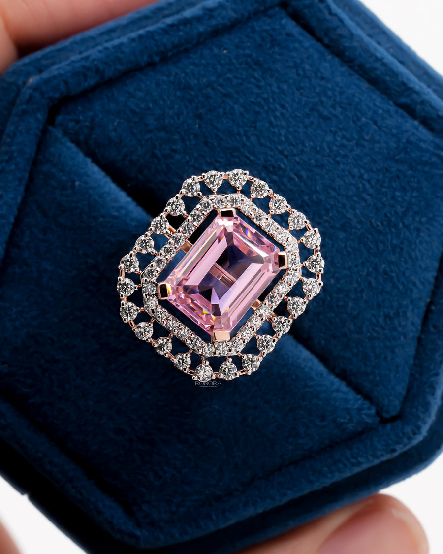 Close-up of a pink emerald cut double halo ring in rose gold in a blue velvet ring box, top view
