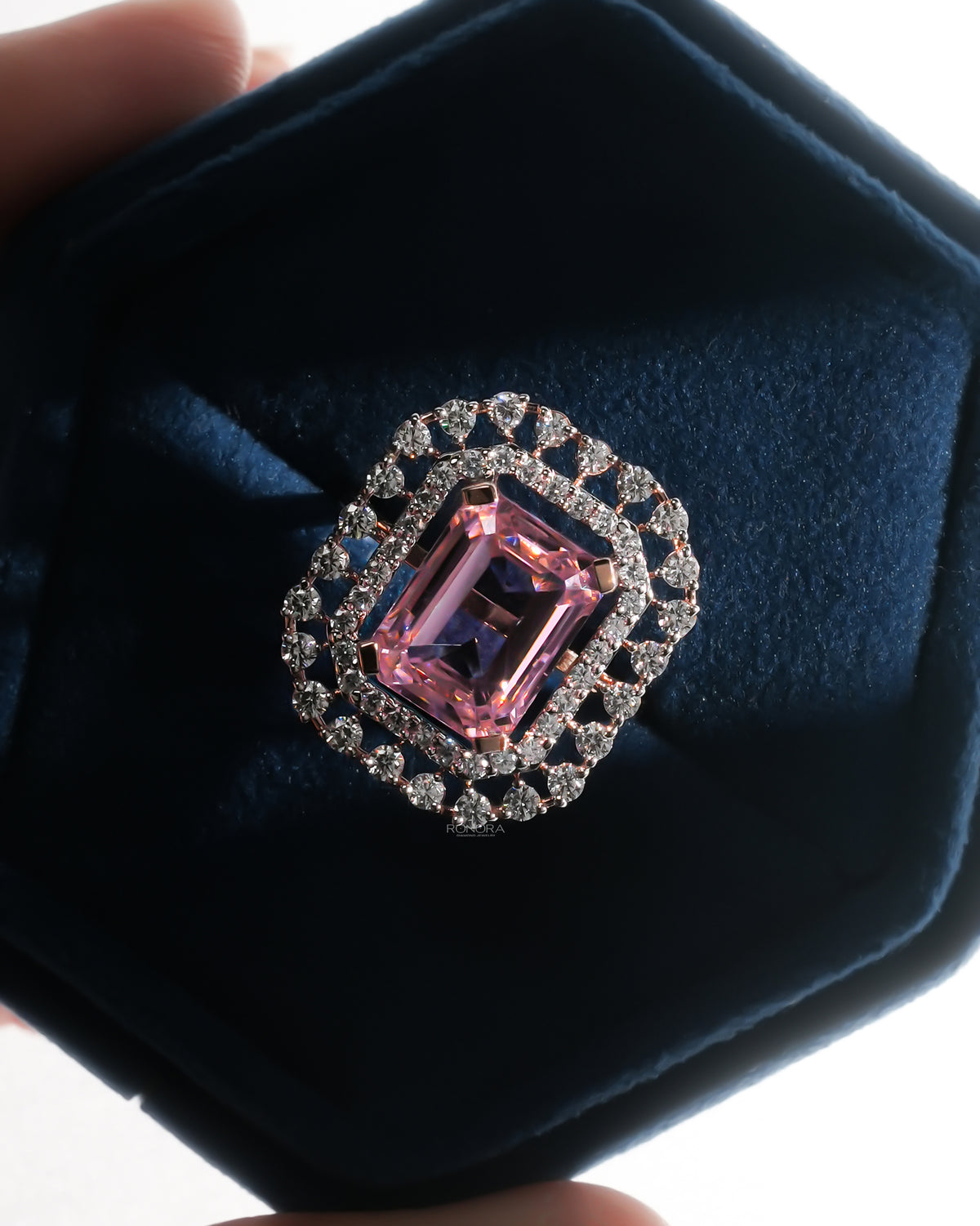 Pink emerald cut double halo ring in rose gold in a dark blue velvet ring box, top view